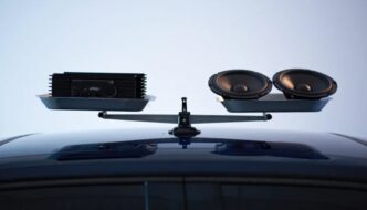 A balanced scale on top of a car with an amplifier on one side of the scale and two speakers on the other