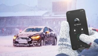 A person's hands pressing the start button for a remote start on their phone for their car which is covered in snow on a cold day
